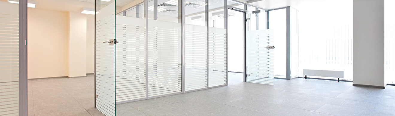 Leere Büroetage mit Glaswänden in Kiel, rahmenlosen Glastüren, Sichtschutzstreifen, grauem Boden, viel Tageslicht, minimalistisches Design.