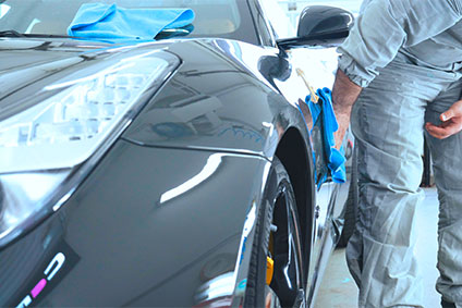 Ein Mann in einem speziellen Anzug poliert einen graues Auto, mit einem blauen Lappen, und verwandelt es in ein Meisterwerk.