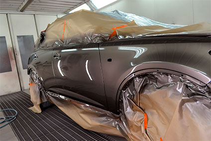 Lackieren eines Autos in einer Werkstatt für Karosseriereparatur. Das Auto ist mit Papier bedeckt um es vor der Farbe zu schützen.