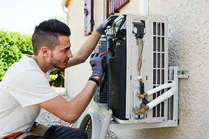 Junger Elektriker installiert bei einem Kunden von außen eine Klimaanlage.