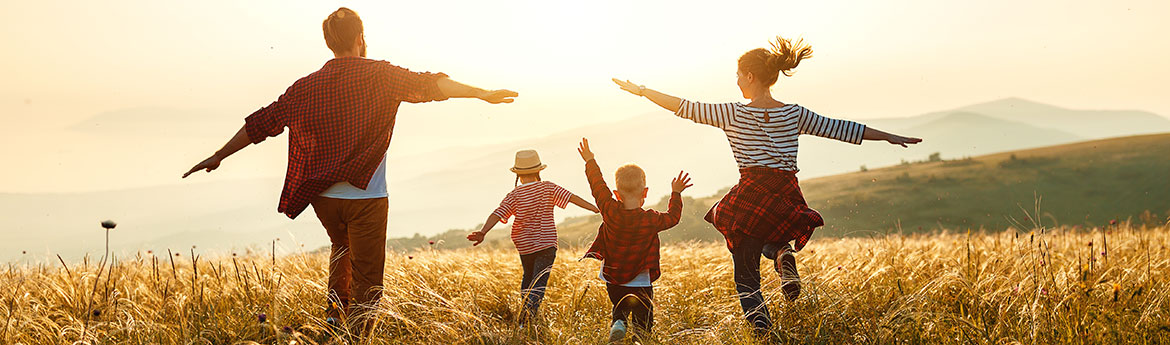 Glückliche Famile, Mutter, Vater und Kindern laufen über eine Wiese im Sonnenuntergang.