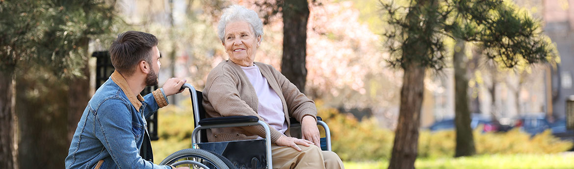 Ältere Frau im Rollstuhl mit jungem Mann im Park.