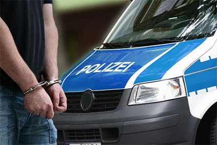 Krimineller Mann mit Handschellen vor einem Polizeiauto