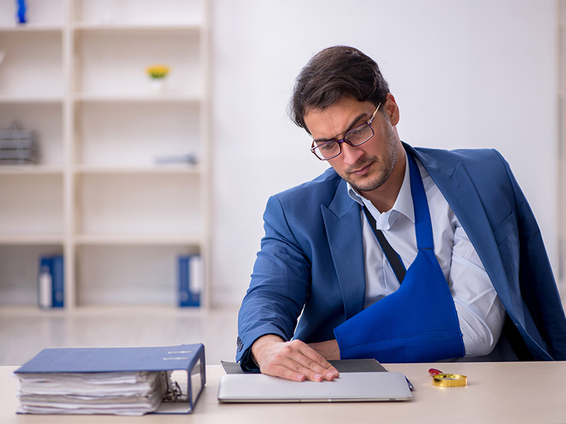 Mann nach Autounfall verletzt am Beratungstisch vom Rechtsanwalt für Verkehrsrecht in Kiel sitzend, Schmerzen haltend, möglicher Anspruch auf Schmerzensgeld nach Unfall und Verletzung.